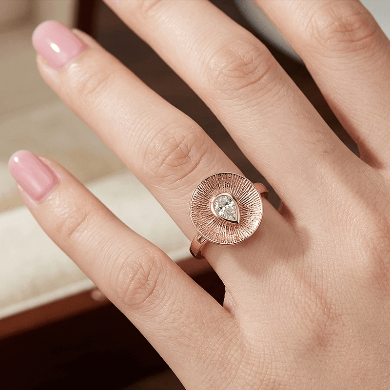 Adjustable open shank rose gold ring featuring a brilliant pear shaped moissanite stone.